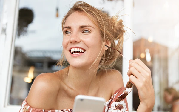 Young woman smiling while holding a clear Invisalign aligner
