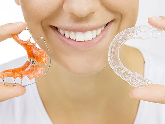 Patient holding a Hawley retainer and a clear retainer after braces treatment